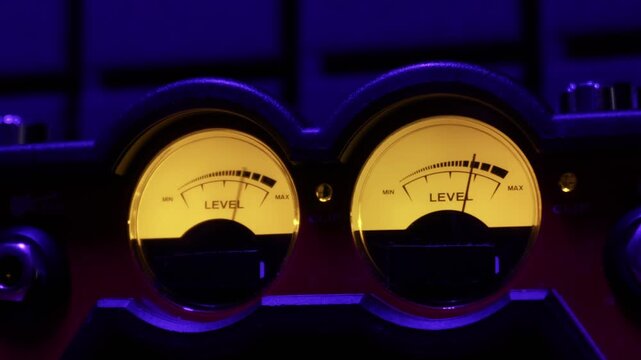 Backlit analog VU meters with fluctuating needles measure audio signal levels. Concept of music production, sound engineering, professional recording, and vintage technology.