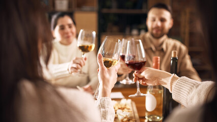 Friends toasting wine glasses at cozy table during evening gathering. Concept of wine advertising,...