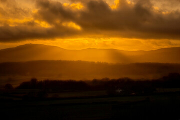 Fototapeta premium Cloudy dark sunset, silhouetting mountains, woods and hills; featuring Moel Famau. Clwydian Hills, Clwyd, Wales