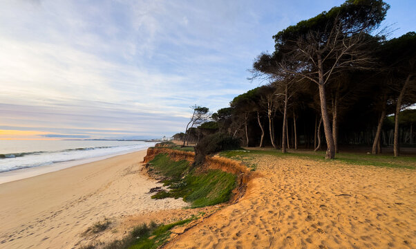 Beautiful sandy beach with red rocks and cliffs. Sunset at dusk with shallow waves on the Atlantic coast in Praia de Loule Velho, Algarve, Portugal