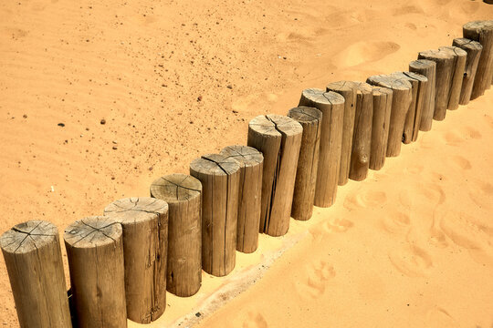 Wooden log border embedded in sand dune, illustrating coastal erosion control and landscaping along a beach path.
