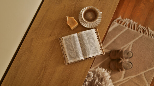 Cozy morning scene with open book, coffee, and candle on a wooden table