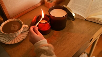 Cozy evening scene with a hand lighting a candle next to coffee and a book