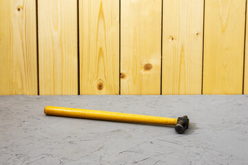 Hammer with wooden handle rests on plaster surface in front of vertical wooden boards. Tool head and handle show wear.