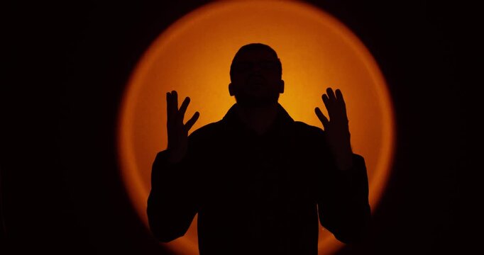 Dramatic front-facing silhouette of a man raising open hands in confusion or frustration against a warm orange circular backlight. Ideal for concepts like uncertainty, stress, crisis, questioning, and