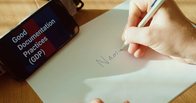 Close-up of a hand writing &ldquo;Name, ID, Date&rdquo; on a document while a smartphone displays &ldquo;Good Documentation Practices (GDP).&rdquo; Ideal for compliance training, regulated recordkeeping, audit readiness, and