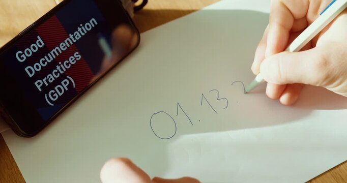 Close-up of a hand making an incorrect documentation correction by heavily scribbling over the entry, while &ldquo;Good Documentation Practices (GDP)&rdquo; is shown on a smartphone. Ideal for compliance training