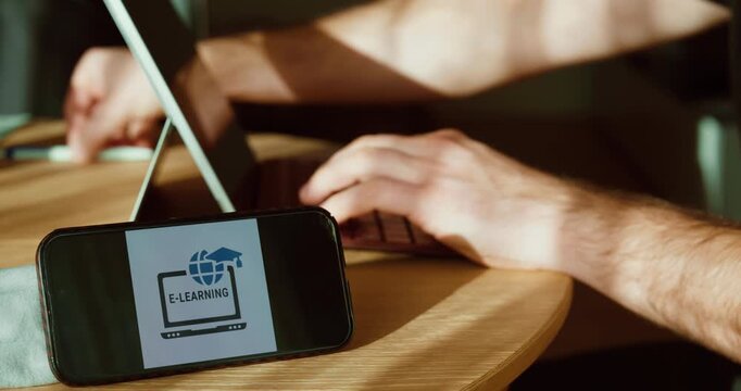 Close-up of a smartphone showing an e-learning screen next to a laptop while hands type, illustrating remote training and digital education at home or in the office. Ideal for corporate learning, comp