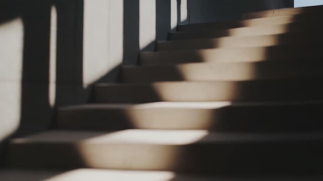 Modern concrete stairway illuminated by strong sunlight streaming through a window, casting dramatic geometric shadows across the steps and wall, symbolizing progress and future