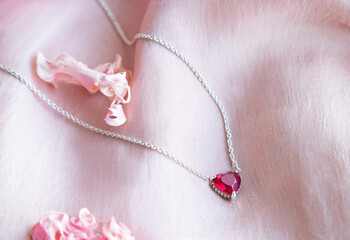 Jewelry. Metal chain (necklace) with stylish pink heart pendants on soft silk fabric. Rose petals creating, tender, romantic atmosphere. Valentine's day,  mother's, woman's day, love holidays.