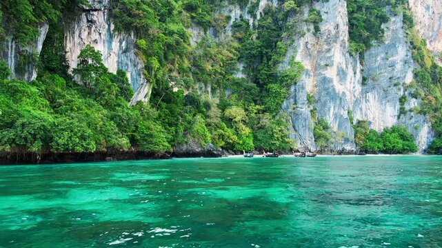 Four traditional thai longtail boats are resting in the calm turquoise water of Monkey Bay. With lush vegetation and limestone cliffs in the background. Located in Phi Phi Don Island. Krabi. Thailand