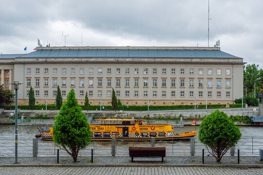 Water Taxi cruising along the Oder River. Directly behind it sits the imposing, neoclassical facade of the Lower Silesian Voivodeship Office (Urząd Wojew&oacute;dzki), Wrocław, Poland.