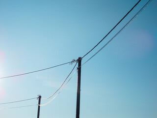 Ice-covered power lines on utility poles against a clear blue winter sky