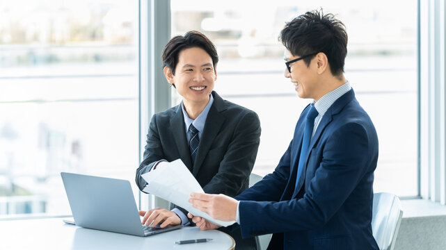 資料を確認しながら打ち合わせをする日本人ビジネス男性2人, Two Japanese business men reviewing documents during a meeting