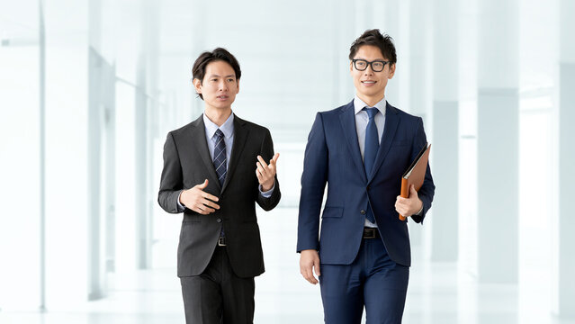オフィス内を歩きながら打ち合わせをする日本人ビジネス男性2人, Two Japanese business men discussing work while walking in an office corridor