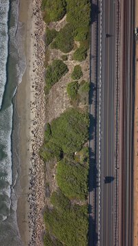 Cars drive on highway 1 in California next to the ocean. Vertical top down drone video.