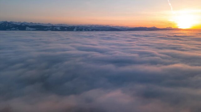 Drone flight at sunset over a sea of ​​fog. Aerial view in the Swiss Alps. The mountain ranges are visible in the background. It is winter. Hyperlapse in a beautiful natural landscape.