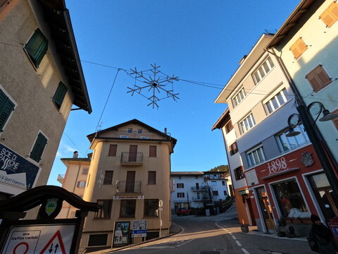 Christmas Decoration Snowflake Hanging over Street in Italian Alpine Town with Historical Buildings and Blue Sky Folgaria