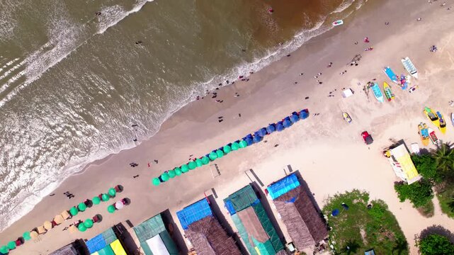 Beach shore line with peoples, sunbeds and shacks at colva, goa, india. day time, top down shot, orbit shot, drone shot, 4k.