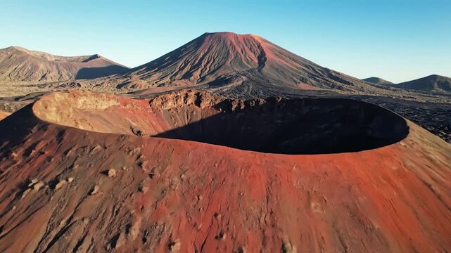 Aerial view showcases a volcanic landscape, featuring a large, red caldera and smaller peaks