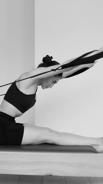 Monochrome video shows fit woman performing seated body tilts and lifts on spring powered Pilates equipment. Sliding base and arm extensions emphasize muscular effort endurance coordination 