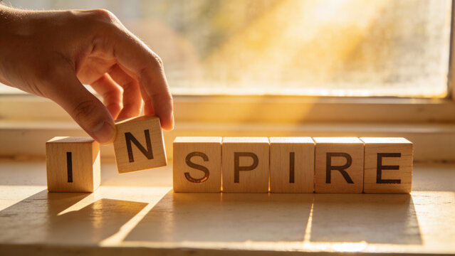 Hand Placing Wooden Block to Spell "INSPIRE" at Sunrise