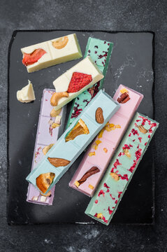 Assorted colorful craft chocolate bars with dried fruits and nuts on dark stone background artisan gourmet confectionery