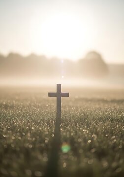 Silhouette of Christian cross in grassy field at sunrise. Resurrection and salvation concept background with golden sun flare.