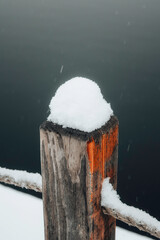 Wooden post covered with fresh snow near water, minimal winter composition and natural textures. © Kamil