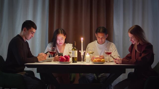 Group friends with cell mobile phone addiction having evening wine dinner together. People celebrating event. Awkward ignore double date problem at restaurant or home. Holiday candle light atmosphere.