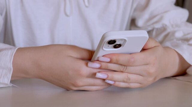 Woman is holding a cell phone in her hand. She is wearing a white shirt