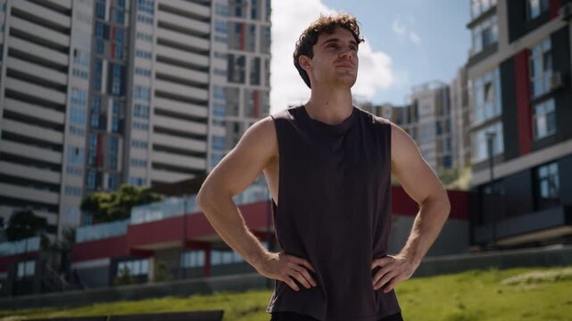 Cheerful motivated Caucasian sport man standing in confident pose strong position looking around stand in city carefree male guy smile proud sportsman relaxing after running jogging workout exercise