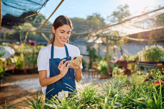 Young florist in a sunny garden center uses a smartphone app to manage inventory, customer orders and small business sales