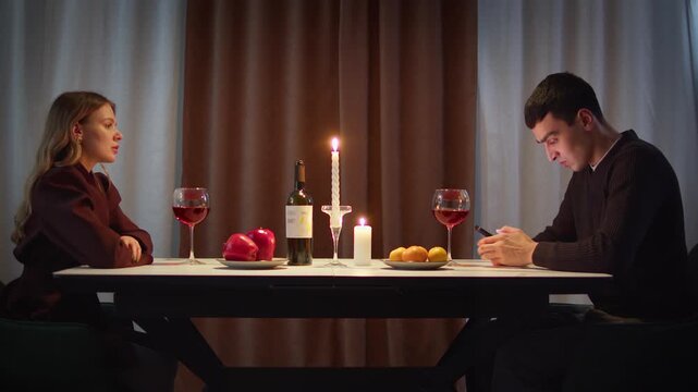 Couple with cell mobile phone addiction having evening wine dinner together. People celebrating event. Awkward ignore romantic first date problem at restaurant or home. Holiday candle light atmosphere