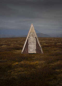 View of a striking triangular structure, weathered and stark, rises from the ochre grasses under a brooding sky, a solitary sentinel, Torshavn, Faroe Islands.
