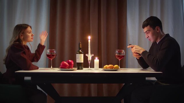 Couple with cell mobile phone addiction having evening wine dinner together. People celebrating event. Awkward ignore romantic first date problem at restaurant or home. Holiday candle light atmosphere