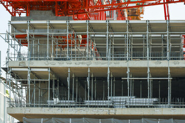 Building under construction with scaffolding and concrete floors, featuring metal beams and crane. structure is in urban setting, showcasing industrial progress