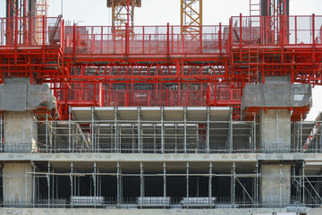Modern construction site with scaffolding and red safety barriers showcases progress of building under construction. structure features concrete pillars and metal frameworks