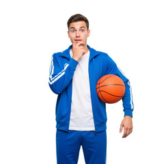 Young Man in Blue Tracksuit Holds Basketball, Hand on Chin &mdash; Thoughtful, Playful, Athletic &mdash; Ideal for Youth Sports, Basketball Culture, or Fitness Strategy Branding.