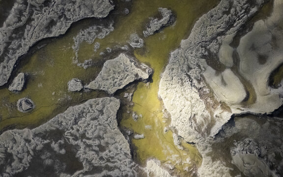 Aerial view of the stark, contrasting landscape where golden waters meet the textured, white earth, creating a surreal and otherworldly scene, Selfoss, Iceland.