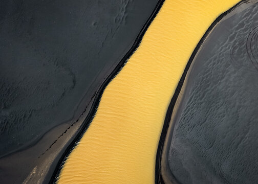 Aerial view of a river of liquid gold winding through dark, textured earth, like a radiant artery pulsing through the landscape, Selfoss, Sveitarfelagid Arborg, Iceland.
