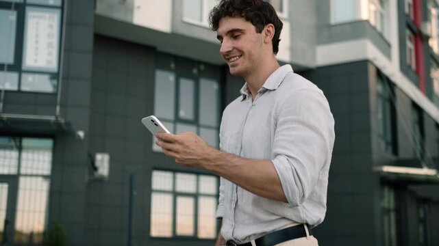 Happy Caucasian business man walking in city downtown looking in mobile phone successful businessman scrolling smartphone walk going near office male employer go outside browsing online application