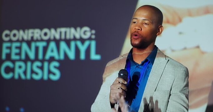 Explaining, stage and man with mic, event and serious for fentanyl crisis, healthcare and speaker. Workshop, presentation and public speaking in seminar, communication and black person with ideas