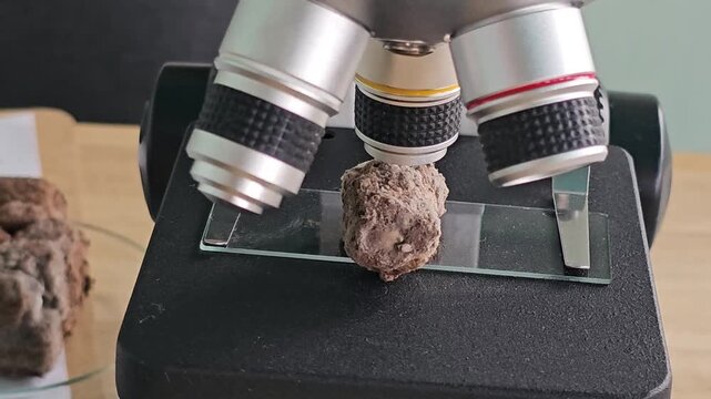 Examining a rock sample under a microscope in a lab setting at a school in the afternoon sun