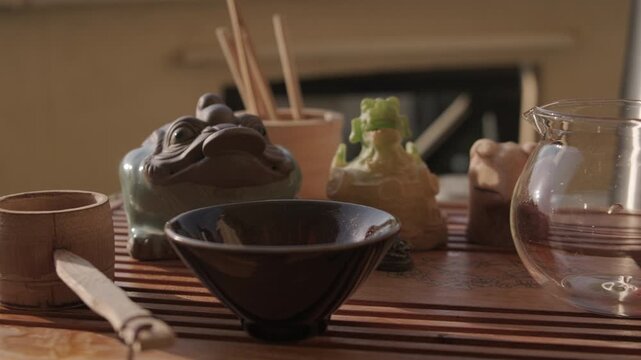 Panning shot of bamboo tea tasting box, glass pitcher, vacuum flask, figurines of tea gods, teabowl and bamboo strainer at tea tray. Traditional chinese gongfu tea ceremony at home balcony