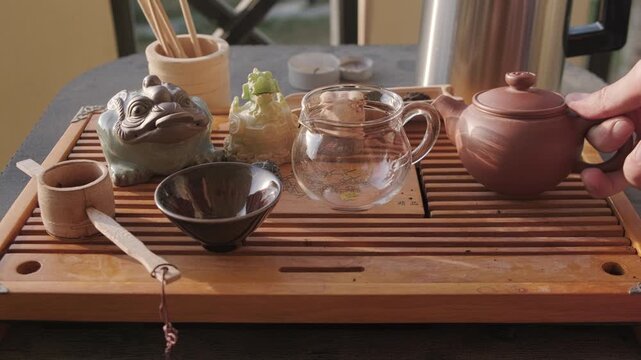 Static footage of gongfu tea ceremony utensils standing at tea tray and hands taking clay teapot out of colorful pouch.