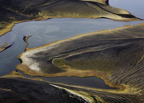 Aerial view of the stark, contrasting landscapes meet water, where black sands intertwine with the blue water, creating a surreal and captivating panorama, Selfoss, Iceland.