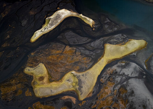 Aerial view of intricate waterways weaving through dark volcanic sands, punctuated by islands of vibrant yellow moss, creating a stark contrast, Selfoss, Iceland.
