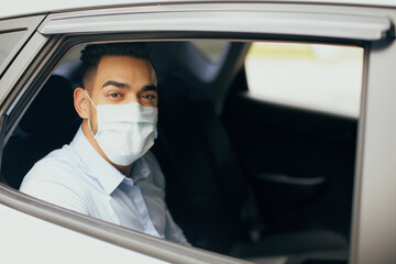 Middle-eastern young man entrepreneur in protective face mask sitting at taxi, going to office while COVID-19 pandemic, closeup portrait, copy space. Arab businessman going to business meeting © Prostock-studio