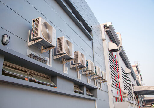 Row of air conditioning compressor units installed on the exterior wall of a modern industrial building.External air conditioning condensers mounted on the wall of a commercial property.